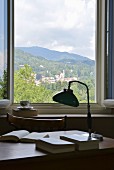View of hills past vintage-style table lamp and books on desk