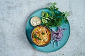 Khao soi soup garnished with red onions, limes, pumpkin seeds and coriander