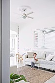 Little girl on bright upholstered sofa in living room with children's play area and colorful garland