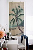 White desk and chair in front of bamboo wall hanging with palm tree motif