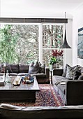 Gemütliche Wohnzimmerecke mit grauer Sofagarnitur vor Fensterfront und Blick auf Bäume