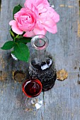 Glass and carafe of wine next to vase of pink roses on vintage wooden surface