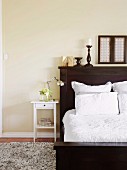 Filigree, white bedside table next to traditional dark brown bed with headboard and white bed linen