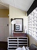 Pallet furniture with tool box and floor lamp in front of wood-clad wall next to louvre window