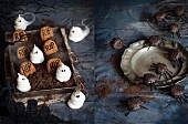 Gebäck zu Halloween: weiße Baiser-Geister und Erdnussbutter-Grabsteine auf Schokoladenmousse-Friedhof, daneben schwarze Sesamspinnen