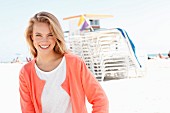 Blonde Frau in weißem Pulli und lachsfarbener Strickjacke am Strand