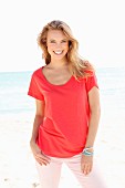 Blonde Frau in rotem Shirt und rosa Hose am Strand