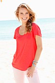 Blonde Frau in rotem Shirt und rosa Hose am Strand