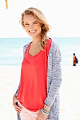 A blonde woman on a beach wearing a red top and a cardigan