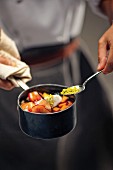 A chef holding a saucepan of fruit comfit