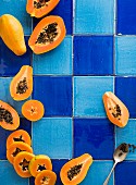Fresh papayas, whole and sliced, on a blue tiled surface