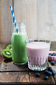 A kale and apple smoothie in a glass bottle and a blueberry and banana smoothie in a glass