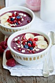 Smoothie bowls made with blackberries, raspberries and banana garnished with banana slices, blueberries, pomegranate seeds, sunflower seeds and oats