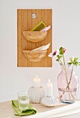 Burning candles in white candle holders and a glass vase in front of a homemade wooden board with bowl-shaped containers