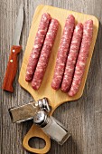 Chipolata sausages on a wooden board with a knife, pepper and salt