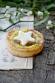 An orange tartlet decorated with a cinnamon star with mistletoe sprigs on a piece of sheet music