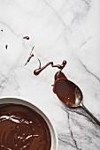 Melted dark organic chocolate in a bowl and spoon on a marble surface