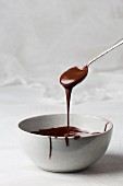 Melted dark organic chocolate dripping from a spoon into a bowl