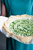 A woman holding a unbaked courgette quiche