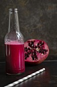 A bottle of pomegranate juice with half a pomegranate in the background