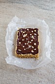 An amaranth bar covered with chocolate and cashew nuts on a piece of paper