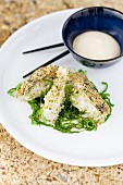 Grilled slices of fish with sesame seed coating on a seaweed medley with a tofu dip