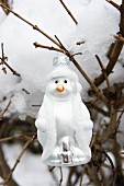 Schneemannanhänger an schneebedeckter am Ast im Garten