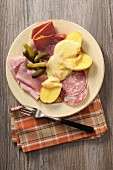 Raclette potatoes with various types of cold meat and gherkins