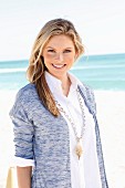 Junge Frau in weisser Bluse und Strickjacke am Strand