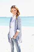 Junge Frau in weisser Bluse, Jeans und Strickjacke am Strand