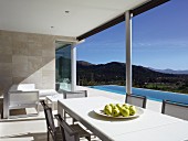 Dining table and chairs on sunny terrace with pool