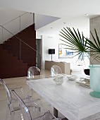 Ghost chairs around crockery and vase of palm leaves on Mediterranean table