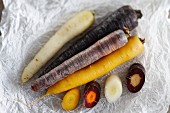 Various different coloured carrots on a piece of white parchment paper