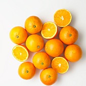 Oranges, whole and halved on a white surface (seen from above)