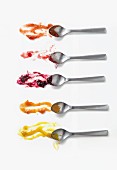 Five different jams on spoons on a white surface