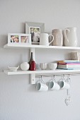 White crockery on a wall shelf with white cups hanging on hooks