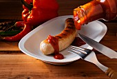 Sausage with ketchup, knife and fork, pepper and chilli peppers, wooden surface