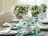 Easter dining table set with white campanula and tealight holders in glass goblets on length of wallpaper used as runner