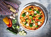 Pizza mit Zucchini, Brokkoli, Pilzen Paprika und Geschirrtuch auf hellem Holz