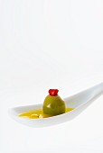 A stuffed olive in olive oil on a white spoon