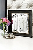 Old mirror with spots, vase of hydrangeas and small perfume bottles on silver tray