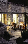Beleuchtete Terrasse mit Gartenmöbeln vor Natursteinfassade