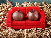 Two handrolled marzipan truffles in dark chocolate with cranberries as coach potatoes on a red sofa