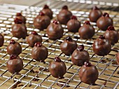Dark chocolate coated, handrolled marzipan truffles with cranberries drying on a wire rack