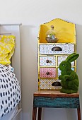 Yellow vintage drawer case with various patterns and green rabbit figure on rustic bedside table in children's room