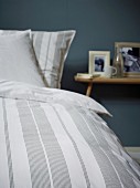 Detail of striped bed linen and bedside table in background