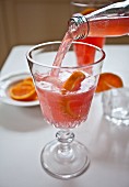 Blood orange lemonade being poured into a glass with ice and citrus fruits