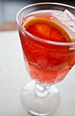 A glass of blood orange soda with citrus slices and ice cubes