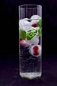 Ice cubes with raspberries and basil in a glass of water