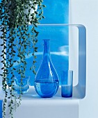 Bauchige Karaffe und blaue Gläser in einem Metallregal mit Hängepflanze